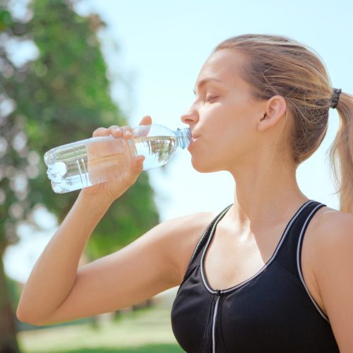 primer-plano-de-una-mujer-joven-bebiendo-agua-contra-el-cielo