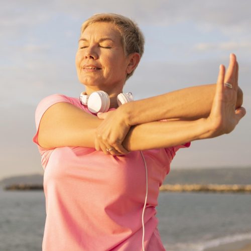vista-frontal-de-mujer-mayor-con-auriculares-extension-en-la-playa